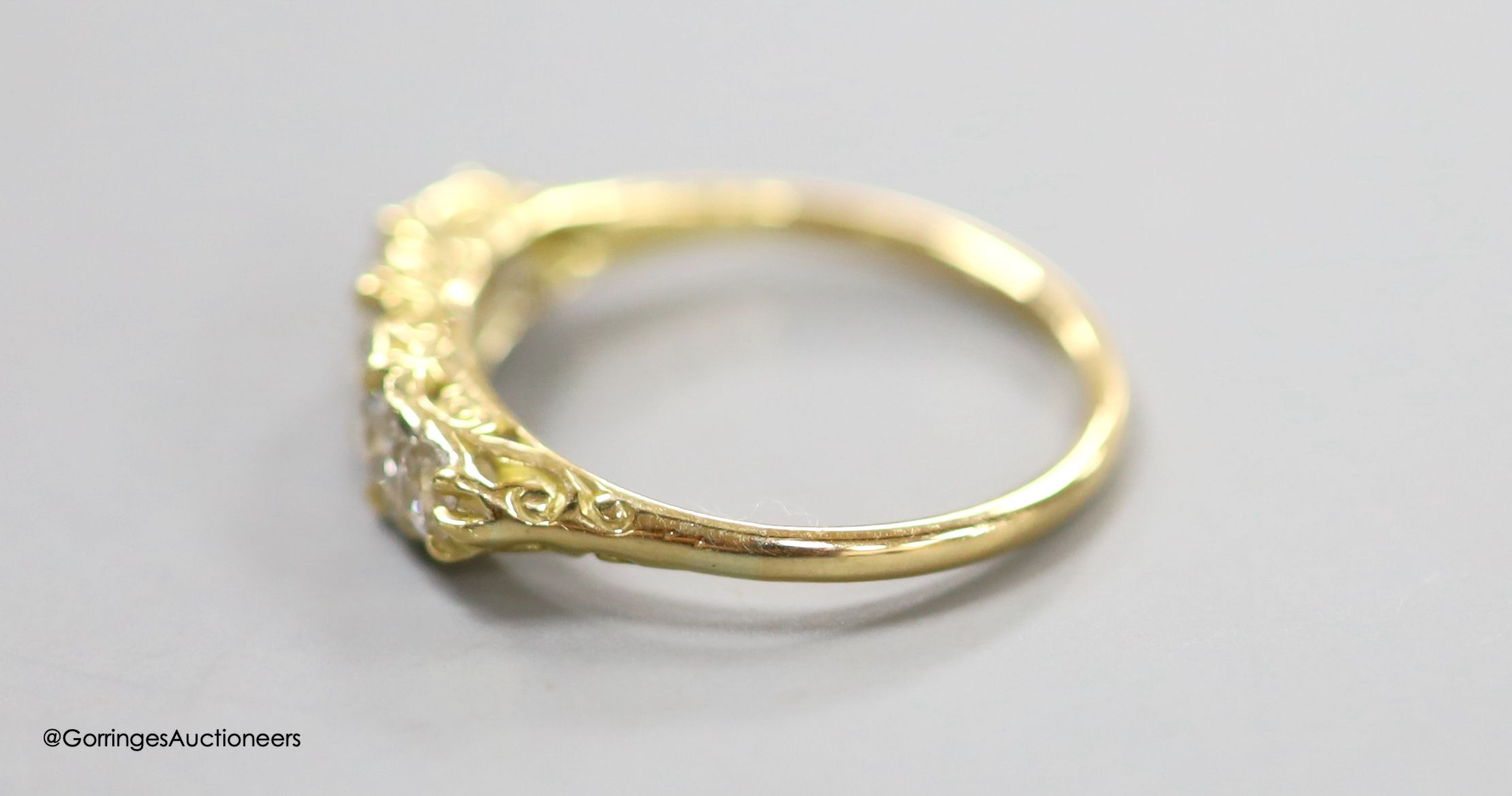 An early 20th century 18ct and graduated five stone diamond set half hoop ring, with diamond chip spacers and carved shoulders, size P, gross weight 2.8 grams